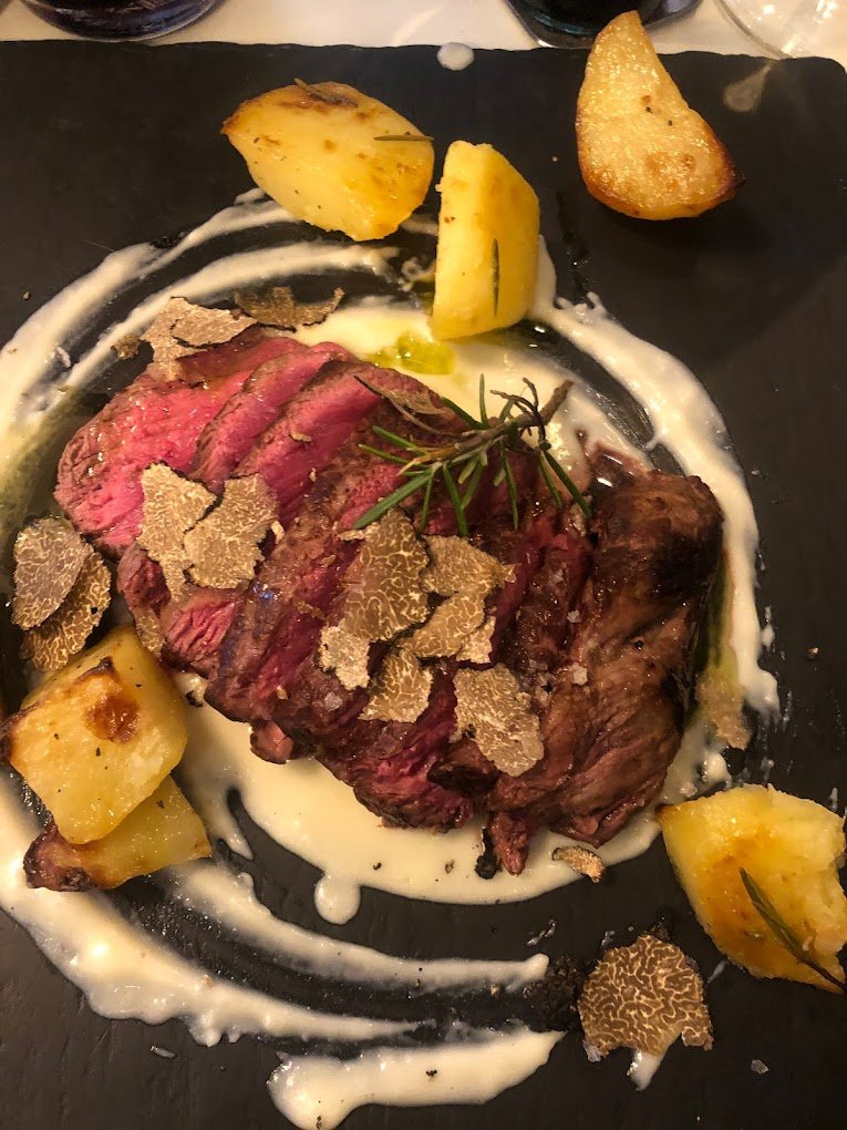 tagliata di manzo servita su letto di fonduta di pecorino e scaglie di tartufo fresco. con patate arrosto