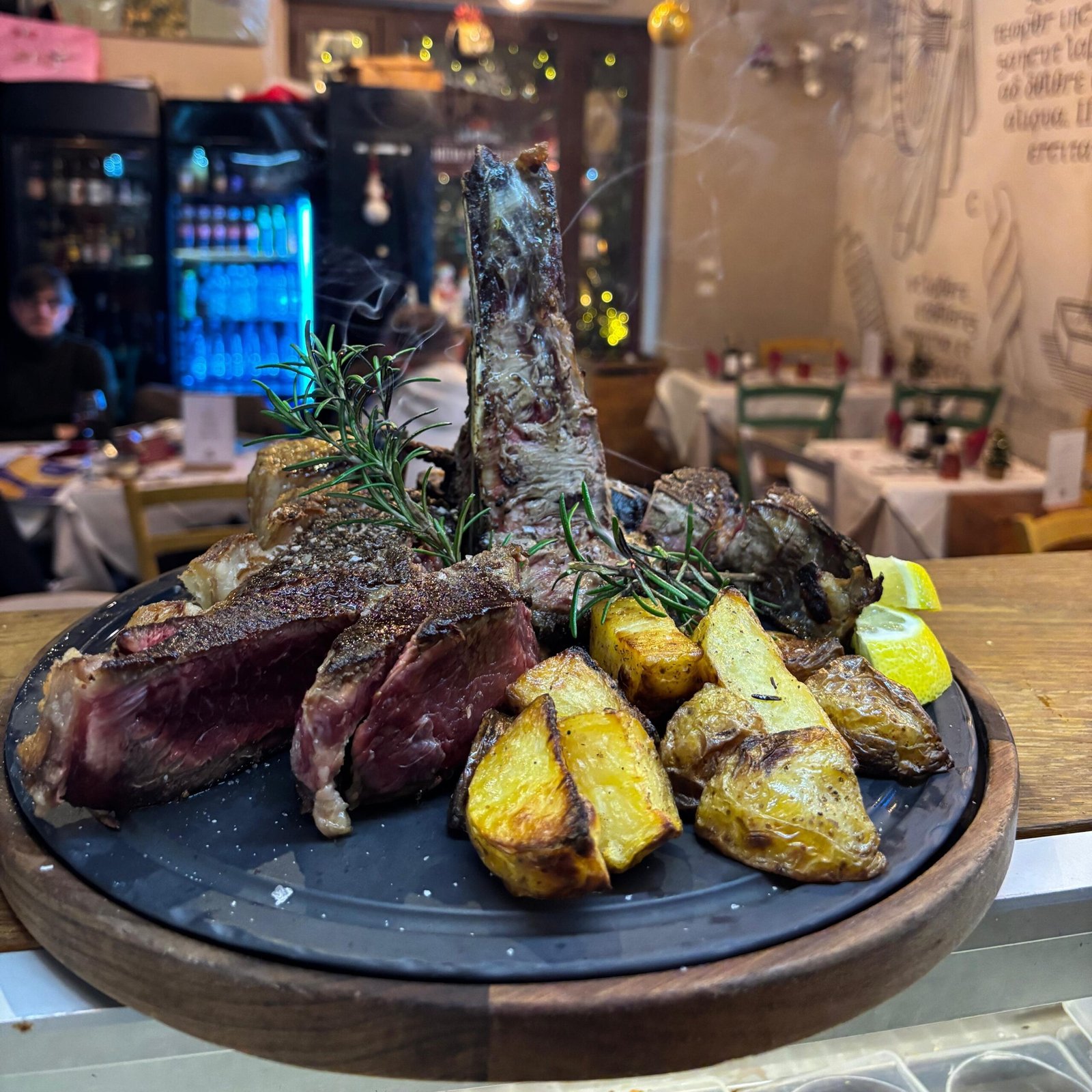 Bistecca alla fiorentina appena cotta servita con patate arrosto, ristorante sullo sfondo